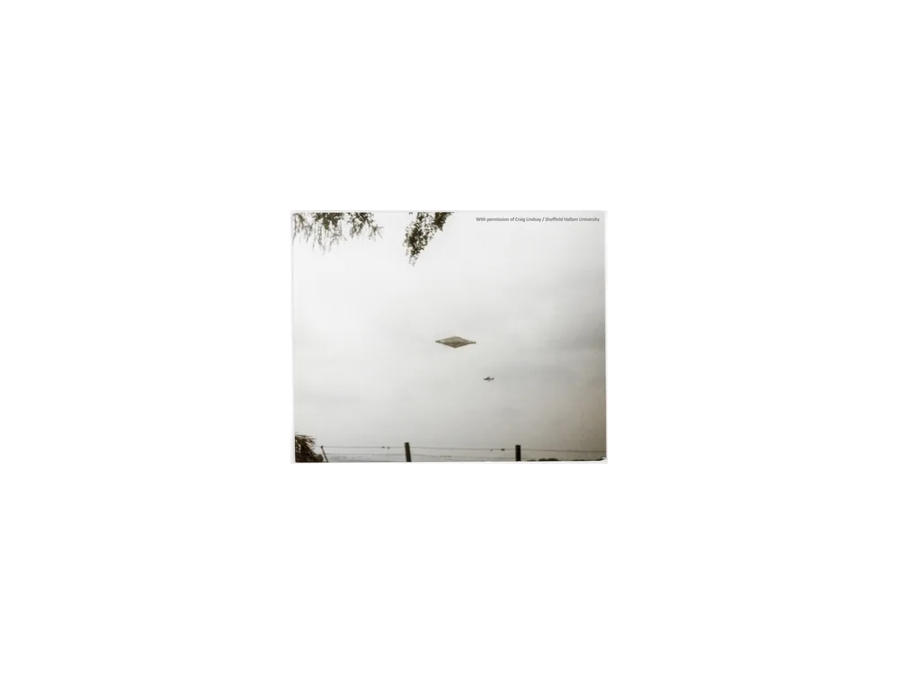 Black and white photograph of a large diamond-shaped object above a treeline.