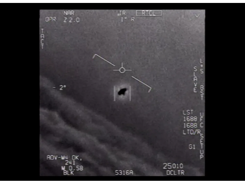 Infrared gun-camera frame showing a dark oval object against cloud, with targeting telemetry overlaid.