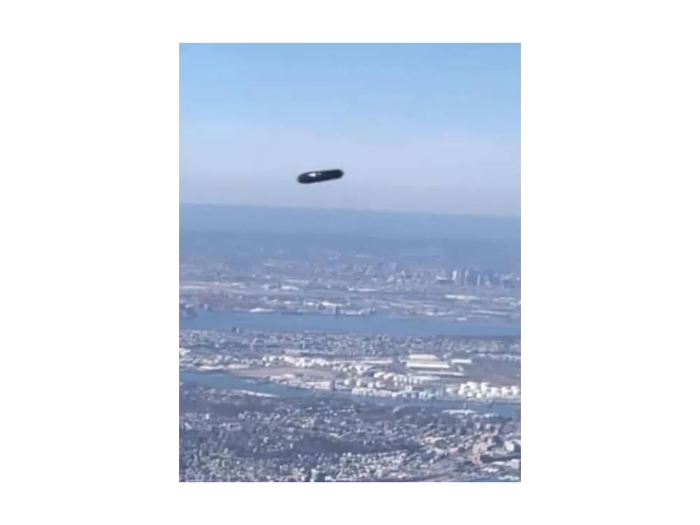 Colour photograph of a dark elongated object above a coastal city and its bay.
